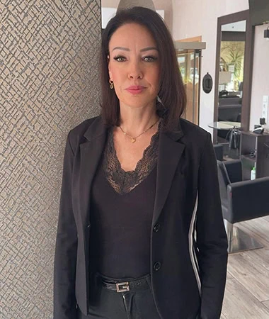 Porträt von Katharina Schan in einer eleganten schwarzen Blazer-Jacke, dezentes Make-up, dunkle Haare, professionelle Salon-Umgebung.